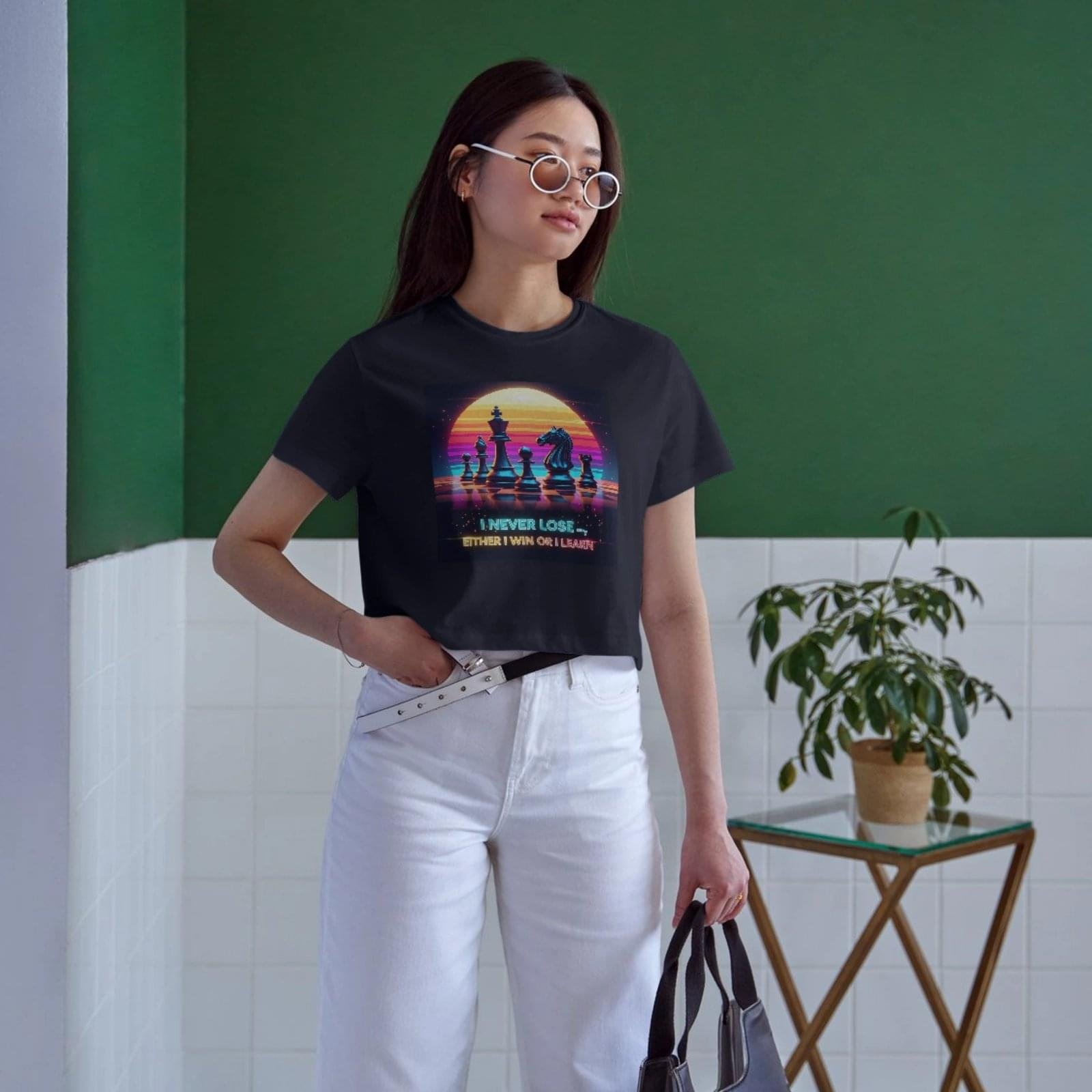 A stylish woman wearing the QGM 'Never Lose' black graphic crop top with white wide-leg pants. The top features a retro chess design and an empowering quote.